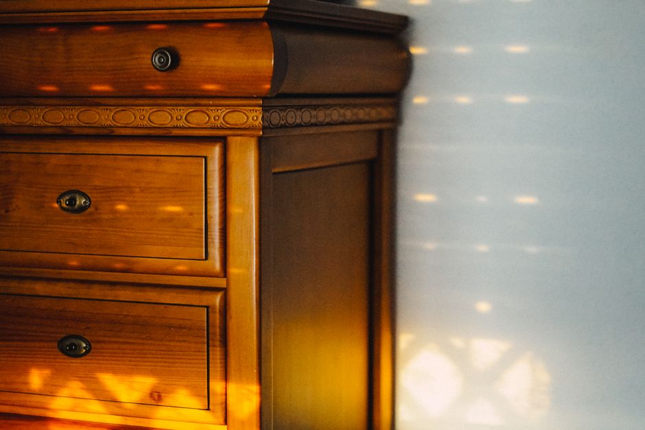 A vintage wooden cabinet with intricate design details illuminated by sunlight casting patterns on the wall.