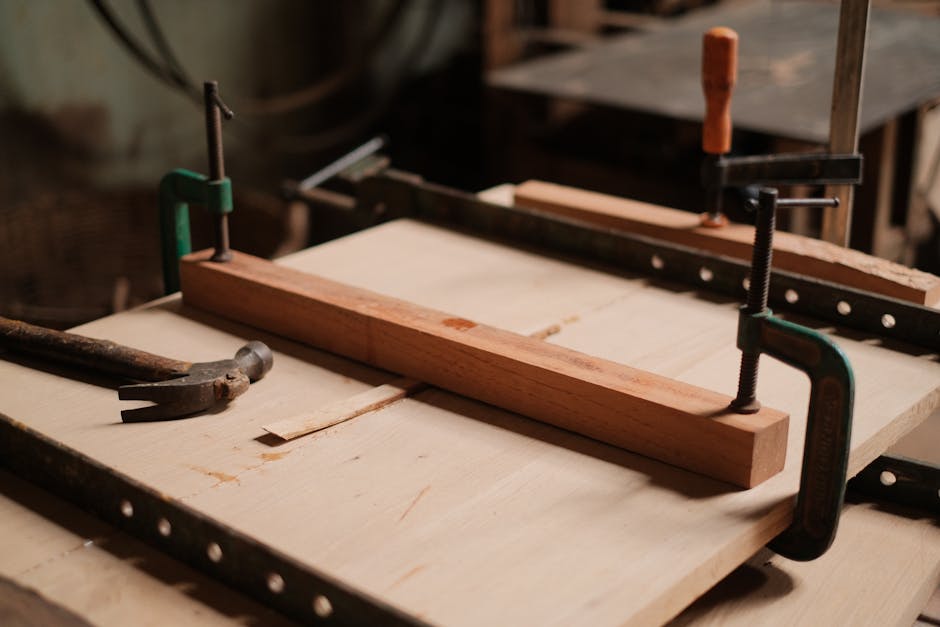 A woodworking workshop scene featuring clamps, a hammer, and wooden planks on a table.